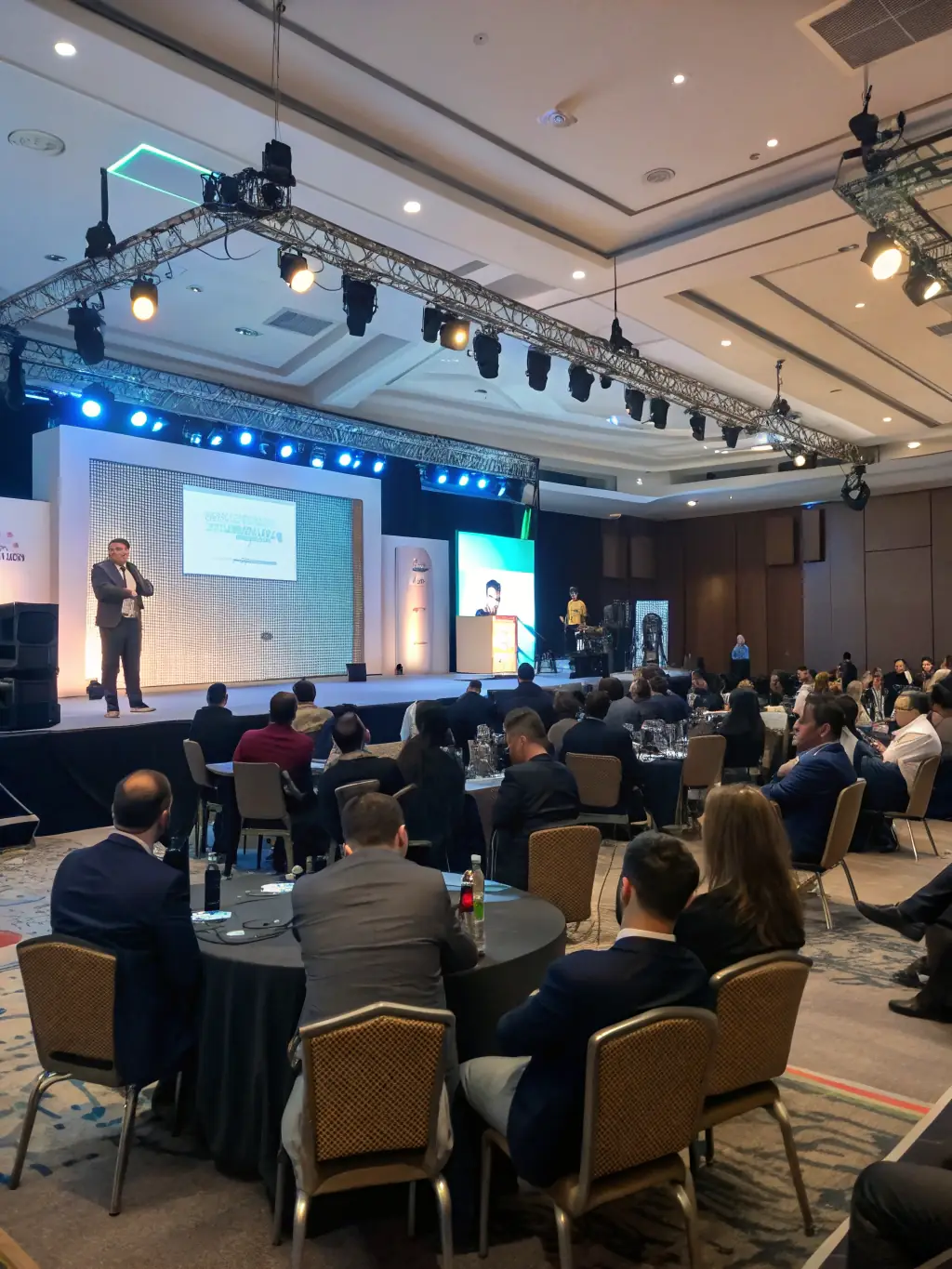 A professional photograph of a conference hall filled with attendees, focusing on a speaker presenting on stage about talent acquisition strategies.